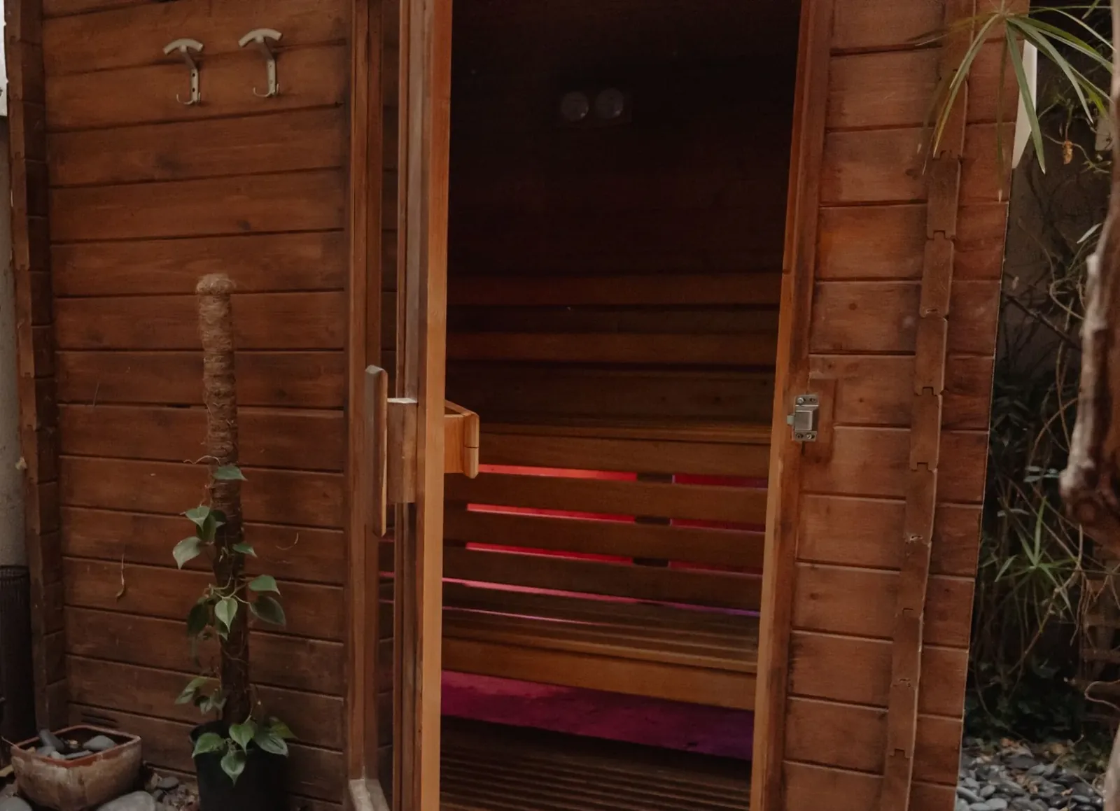 The wooden sauna cabin at Sensation Spa Paris, door open onto red light, plants and pebbles at its foot