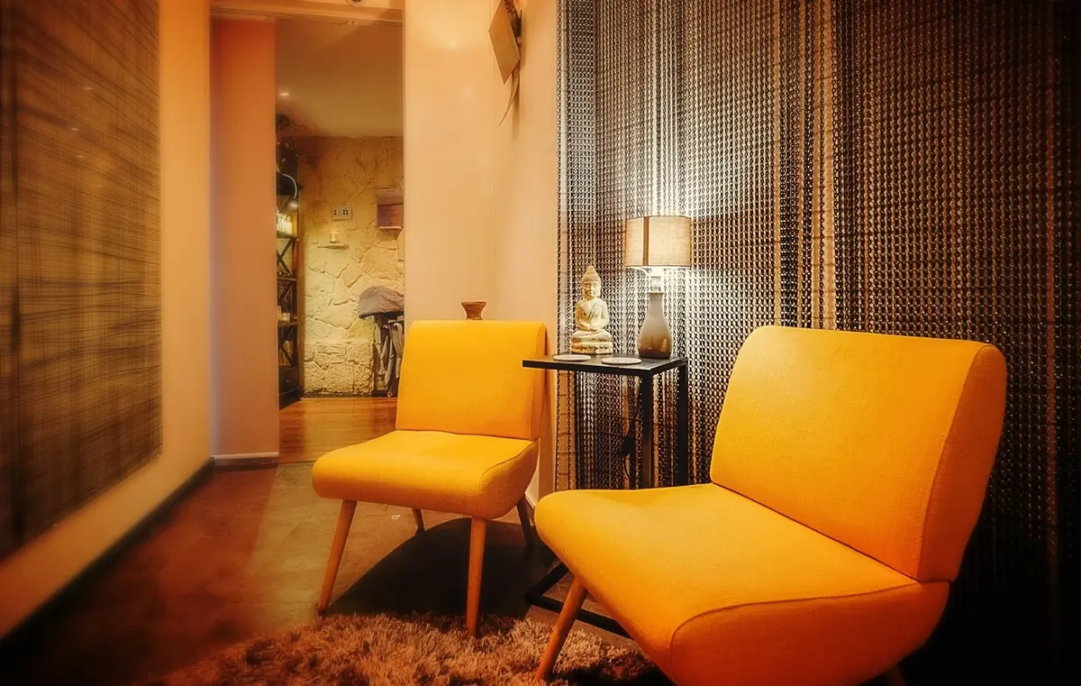The spa's small relaxation corner: two mustard-yellow armchairs, a lamp and a figurine behind a woven curtain